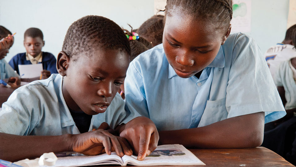 A young boy reading with an older girl, supported by Project Luangwa.
